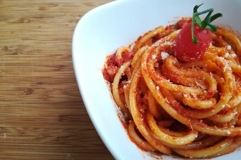 Bucatini i tomatsauce drysset med revet ost i en hvid skål på et træbræt