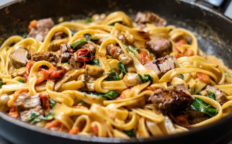 Tagliatelle i en pande med stykker af oksekød, tomater, spinat og svampe