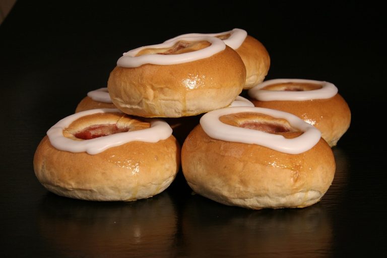 Fastelavnsboller med hvid glasur stablet på et mørkt bord